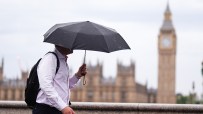 Man with umbrella walking past Big Ben and Houses of Parliament in London on an overcast day.