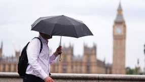 Man with umbrella walking past Big Ben and Houses of Parliament in London on an overcast day.