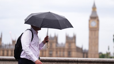Man with umbrella walking past Big Ben and Houses of Parliament in London on an overcast day.