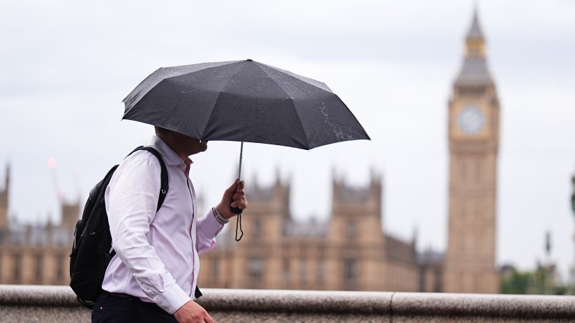 Man with umbrella walking past Big Ben and Houses of Parliament in London on an overcast day.