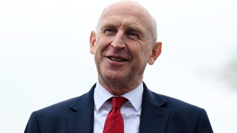 Smiling bald man in a dark suit and a red patterned tie, looking up and to the right.