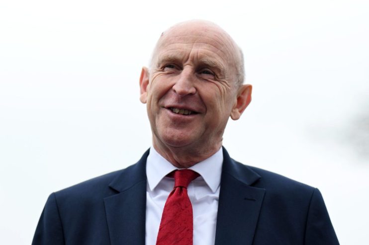 Smiling bald man in a dark suit and a red patterned tie, looking up and to the right.