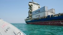 Large cargo ship, Capital One Lines containers visible, on bright blue water, with a small boat in foreground.