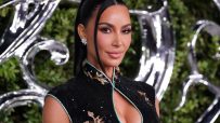 Kim Kardashian in a black sequined dress with a mandarin collar, diamond earrings, and a sleek ponytail.