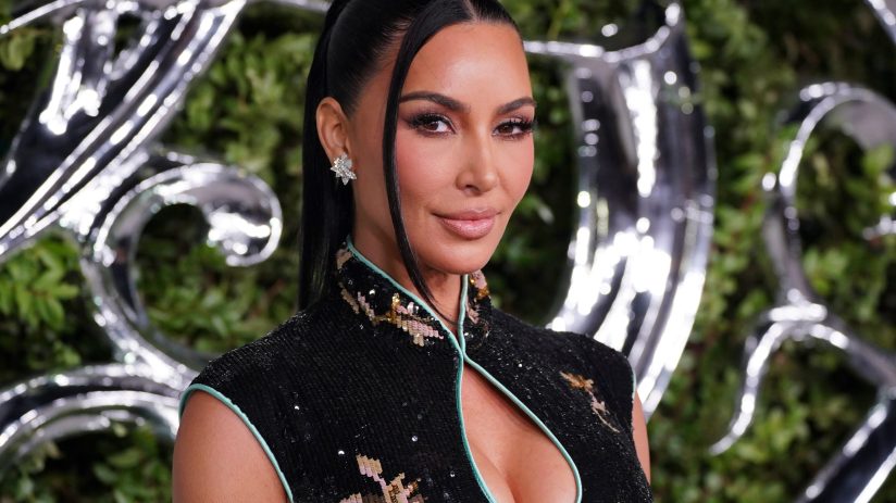 Kim Kardashian in a black sequined dress with a mandarin collar, diamond earrings, and a sleek ponytail.