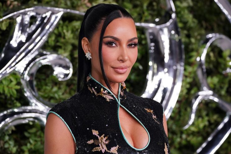 Kim Kardashian in a black sequined dress with a mandarin collar, diamond earrings, and a sleek ponytail.