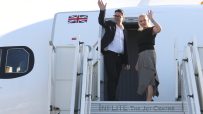 Andy Burnham and a woman waving from the steps of an airplane with a Union Jack flag