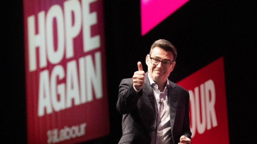 Andy Burnham, Mayor of Greater Manchester, gives a thumbs-up gesture in front of a Hope Again Labour banner.