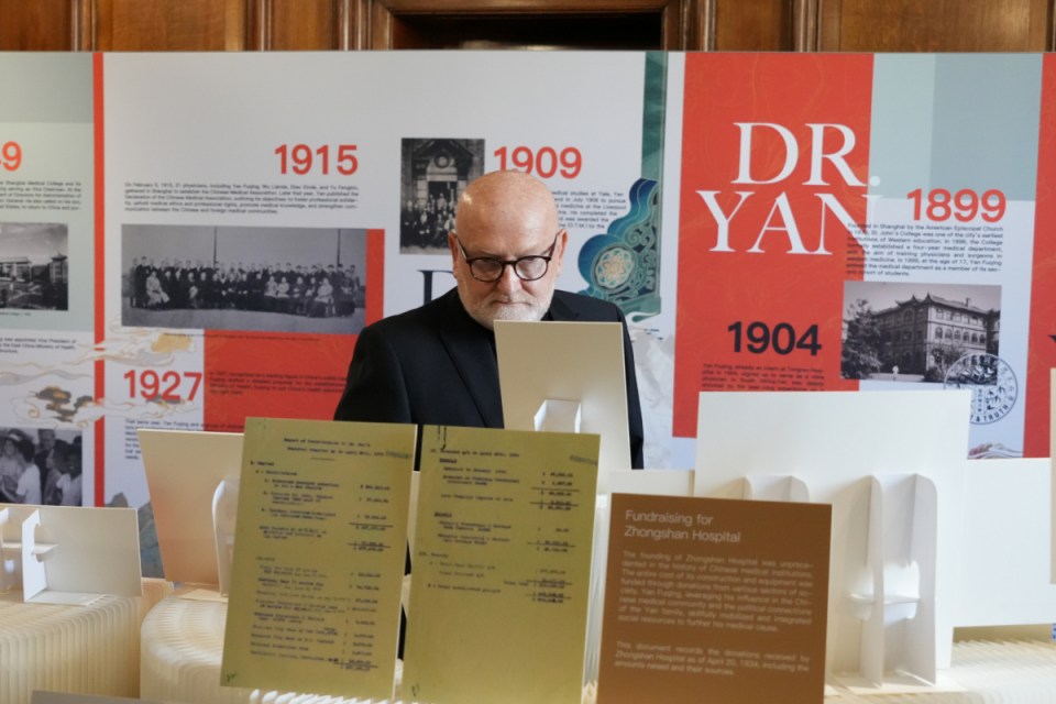 Man in glasses reviewing historical documents on display at an exhibition, with timeline in background