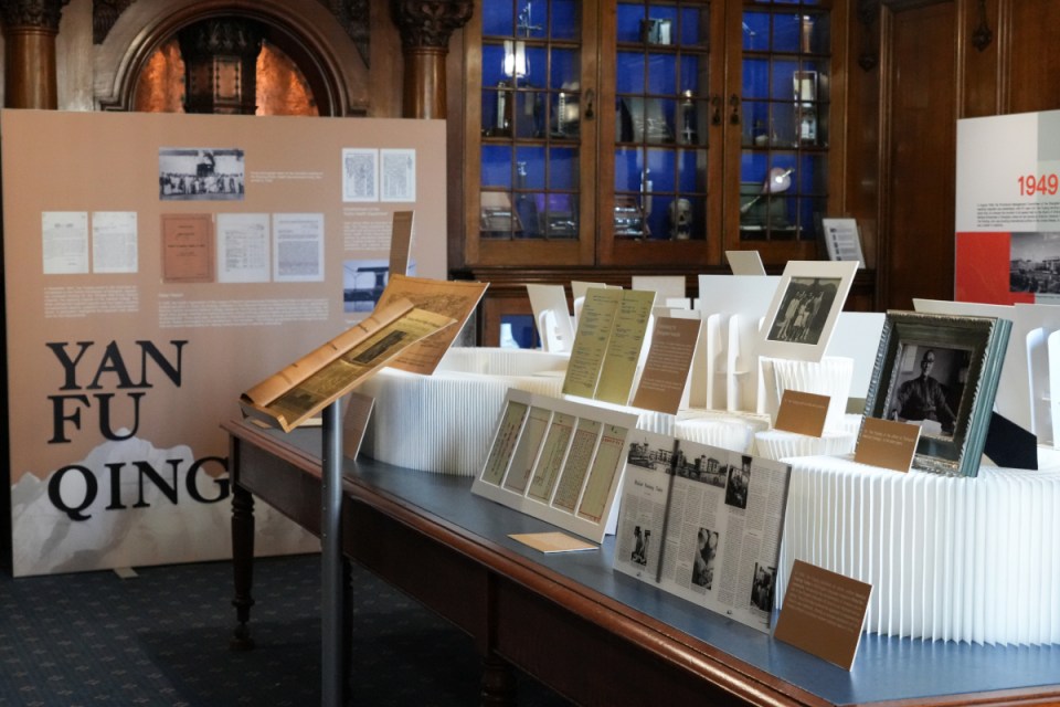 Exhibition scene featuring YAN FU QING display, documents, and historical photos on a long table.