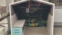 Calm Space booth with a nature mural and light grey bench, offering a quiet retreat in a public area.