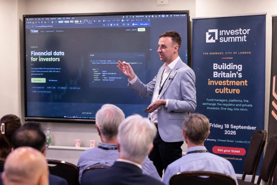 A man presenting financial data for investors on a large screen at the Investor Summit in London.