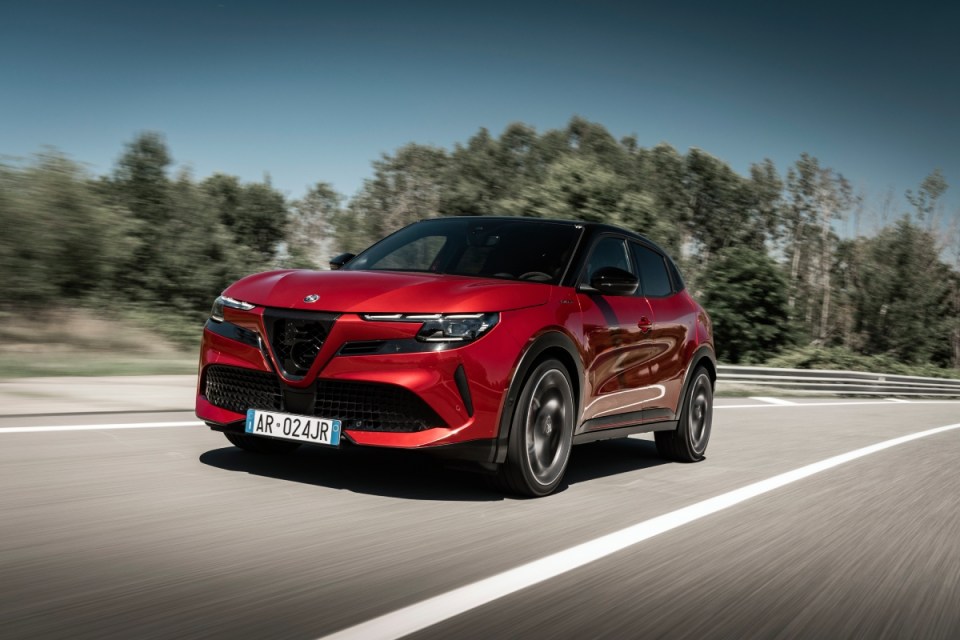 Red Alfa Romeo Tonale compact SUV driving on a highway with blurred background, clear sky.