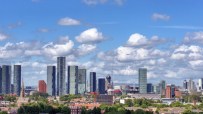 Manchester skyline with modern skyscrapers, residential buildings, and green trees under a blue sky with clouds