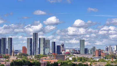 Manchester skyline with modern skyscrapers, residential buildings, and green trees under a blue sky with clouds