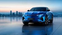 Sleek blue Alpine A390 electric SUV with distinctive headlights, parked on a reflective surface before a city skyline at d...