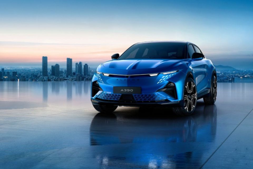 Blue Alpine A390 electric SUV with city skyline in background, reflecting on a wet surface at dusk.