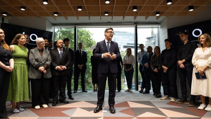 Andy Burnham speaking at Number 10 North, surrounded by a diverse group of attendees in a modern office setting.