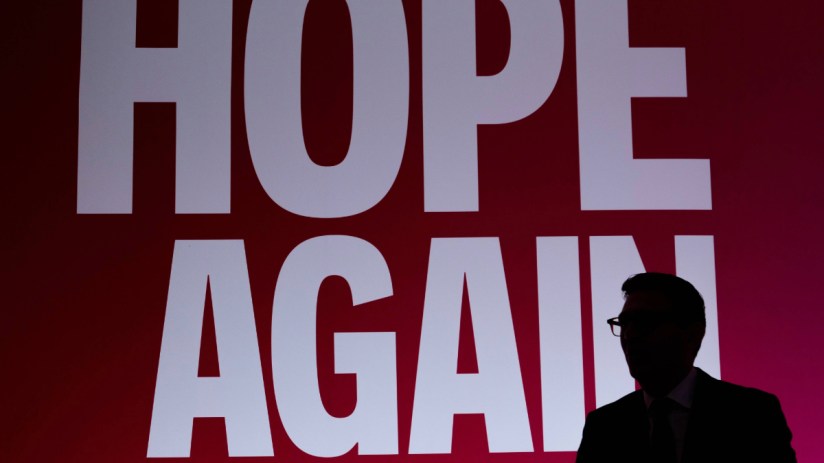 Silhouette of Andy Burnham speaking, with HOPE AGAIN text in white on a red background behind him.