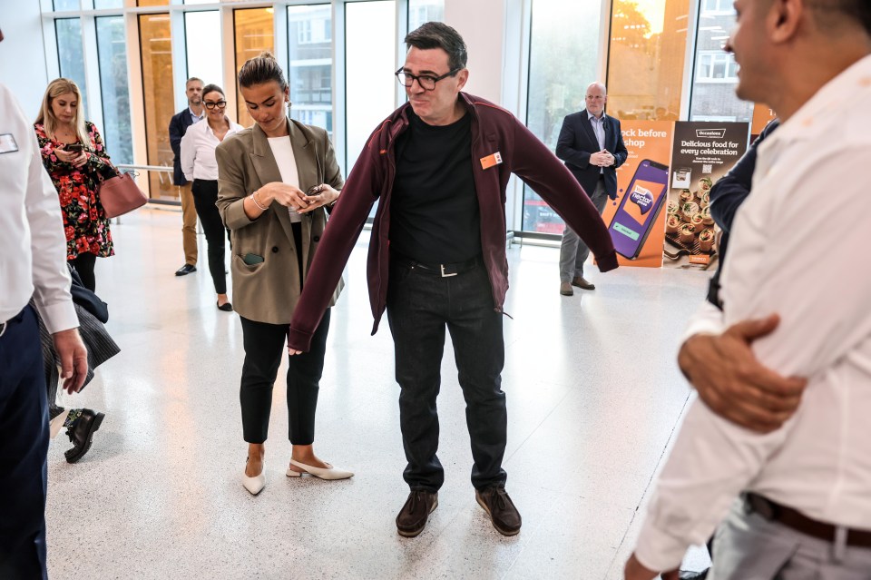 Andy Burnham in a Sainsburys fleece, wearing glasses, at a public event.