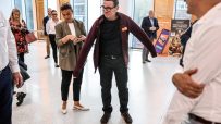 Andy Burnham in a Sainsburys fleece, adjusting his jacket, at a retail event with other attendees.