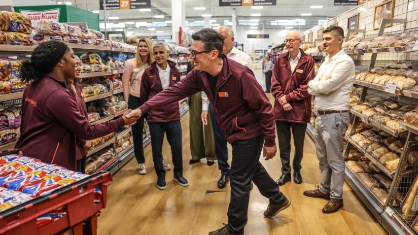 Andy Burnham greets a Sainsburys employee, with Sadiq Khan and others observing in the bakery aisle.