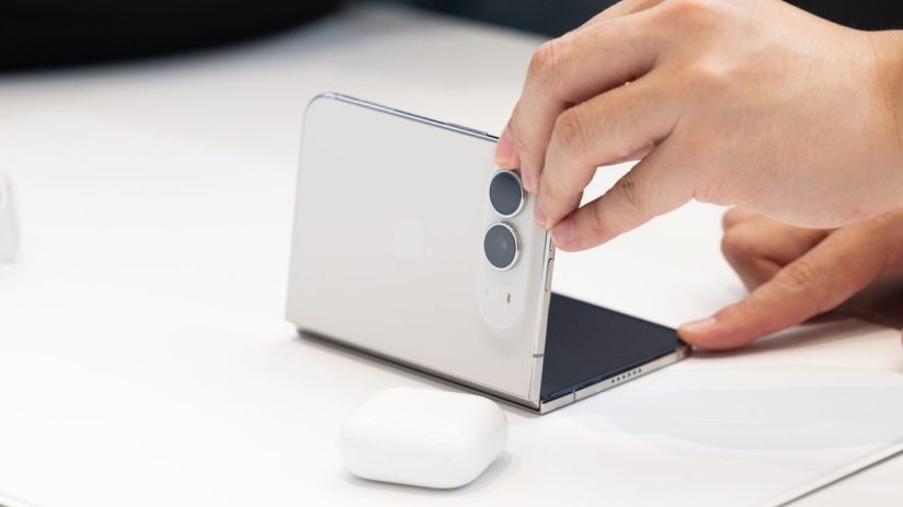 Hand interacting with a white foldable Apple iPhone, showing its dual cameras and partially folded screen
