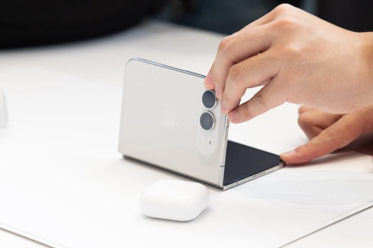 Hand interacting with a white foldable Apple iPhone, showing its dual cameras and partially folded screen