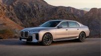 A sleek, silver BMW i7 luxury sedan parked on an asphalt road with rugged mountains in the background.
