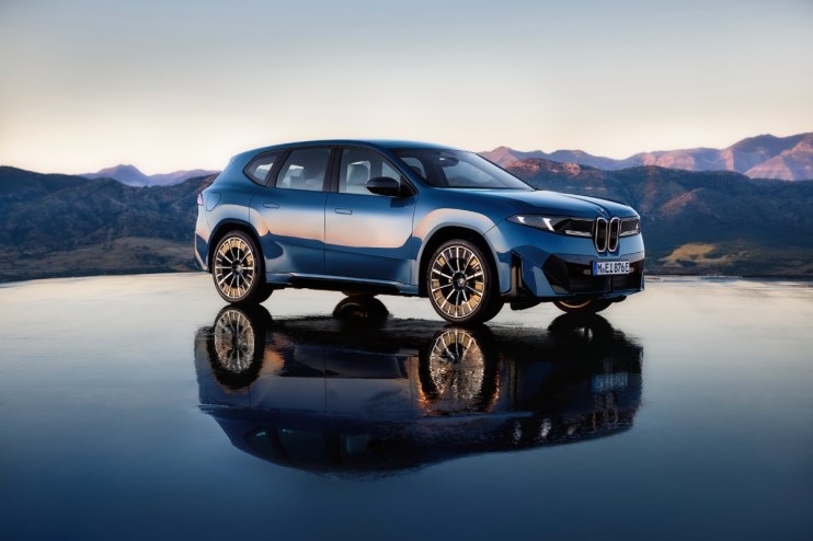 Blue BMW iX3 electric SUV parked on a reflective surface with mountains and sky in the background