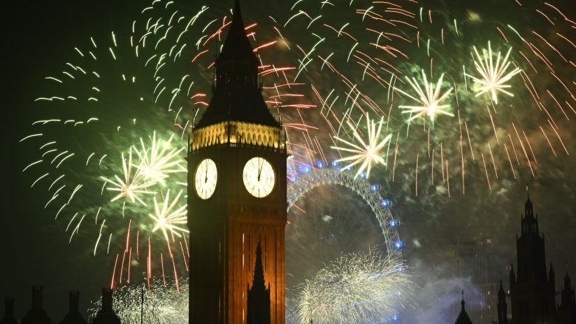 Big Ben and the London Eye illuminated by a vibrant display of green and red fireworks at night.