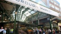 Borough Market entrance with vendors, fresh produce, and shoppers under the iconic green roof structure