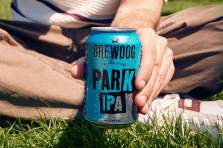 Hand holding a blue BrewDog Park IPA can with condensation, sitting on green grass