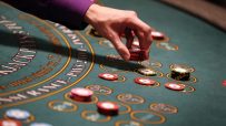 Hand placing red betting chips on a green blackjack casino table with yellow markings