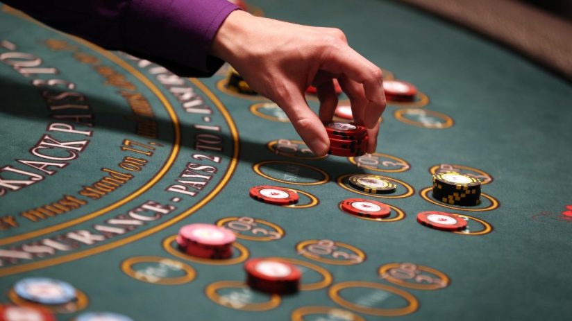 Hand placing red betting chips on a green blackjack casino table with yellow markings