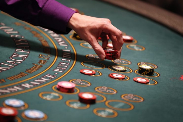 Hand placing red betting chips on a green blackjack casino table with yellow markings