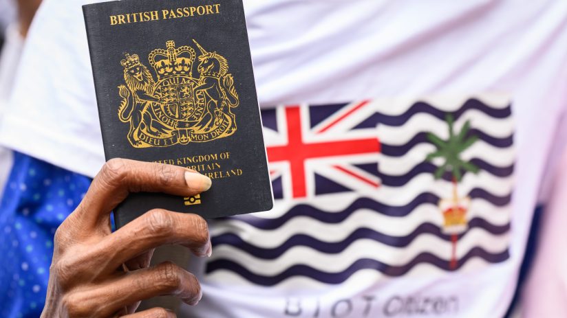 Hand holding a British passport against a shirt with the Chagos Islands flag, symbolizing British sovereignty.