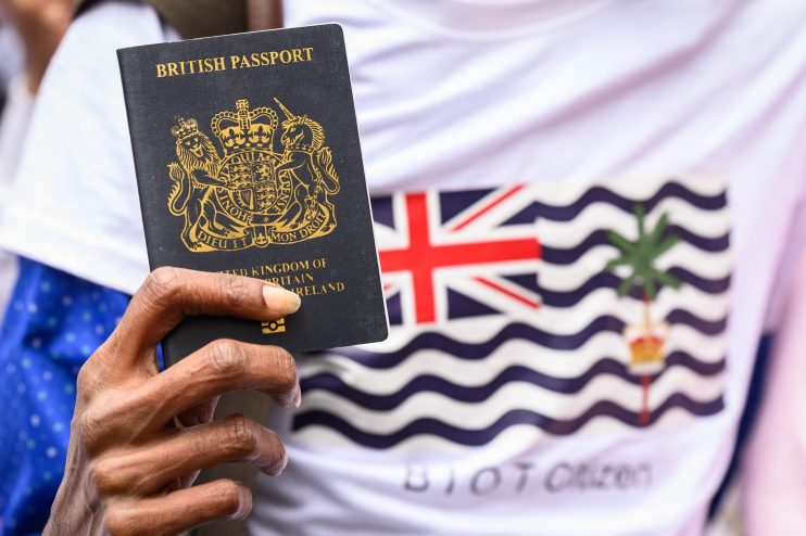 Hand holding a British passport against a shirt with the Chagos Islands flag, symbolizing British sovereignty.