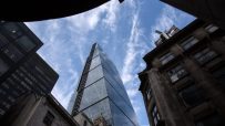 Low-angle view of the Cheesegrater skyscraper in the City of London against a blue sky with wispy clouds.