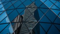 Modern office buildings in the City of London reflected in the geometric glass facade of another skyscraper.