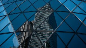 Modern office buildings in the City of London reflected in the geometric glass facade of another skyscraper.