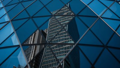Modern office buildings in the City of London reflected in the geometric glass facade of another skyscraper.