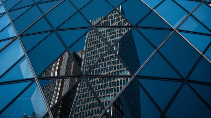 Modern office buildings in the City of London reflected in the geometric glass facade of another skyscraper.