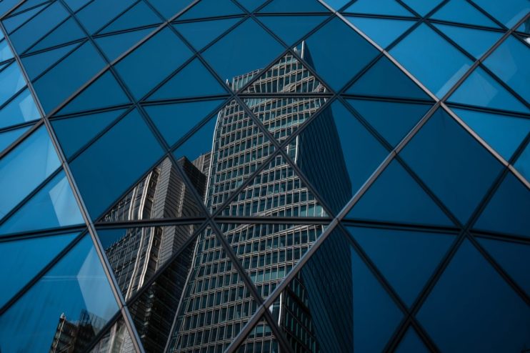 Modern office buildings in the City of London reflected in the geometric glass facade of another skyscraper.