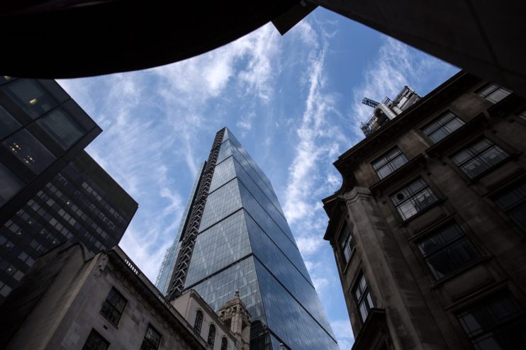 Glass skyscraper rising into a cloudy blue sky, surrounded by dark historic London buildings.