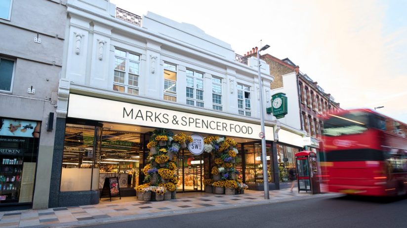 Marks & Spencer Food store in Clapham Junction, London, with a red double-decker bus blurring past.