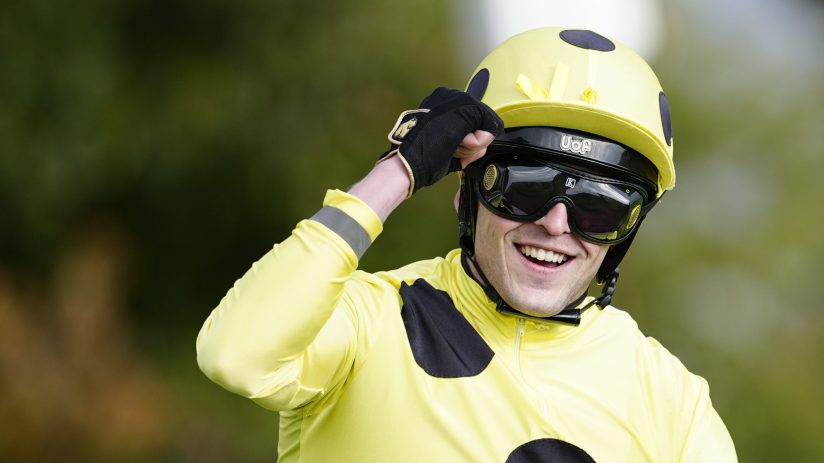 Jockey Clifford Lee smiling, wearing a yellow racing helmet, goggles, and yellow and black silks.