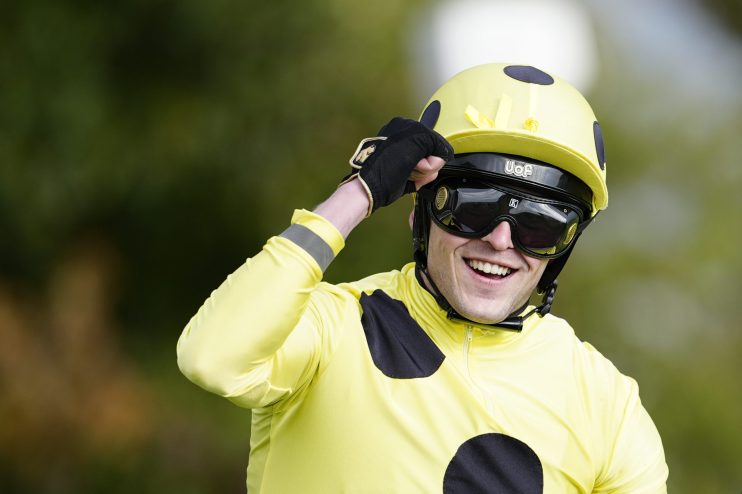 Jockey Clifford Lee smiling, wearing a yellow racing helmet, goggles, and yellow and black silks.