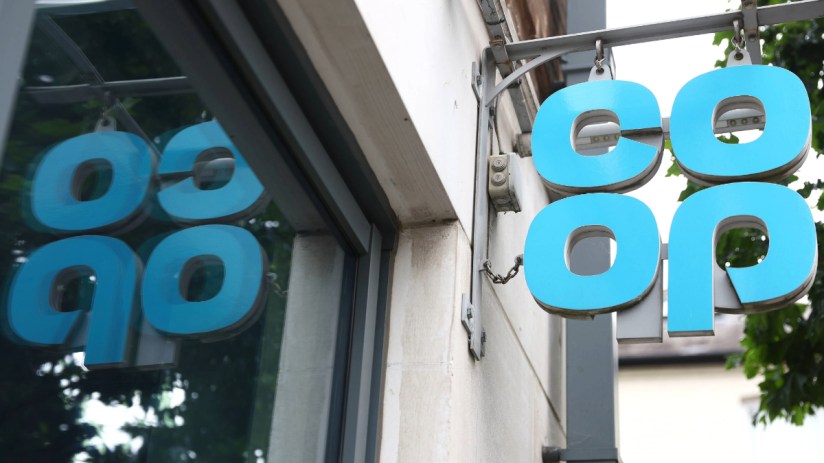 Blue Co-op sign hanging outside a building, with its reflection visible in a window