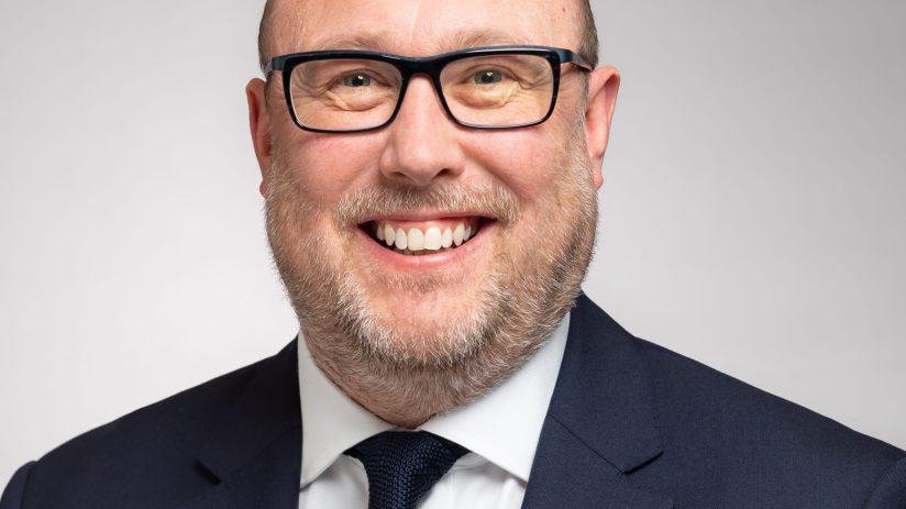 David Bimpson, smiling professional in a navy suit and glasses, white shirt, dark knitted tie